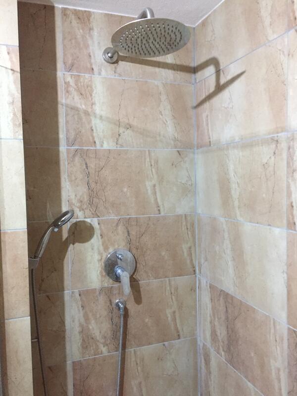 Saniertes Bad: bodengleiche Dusche mit Regenduschkopf und großformatigen Fliesen in Natursteinoptik.
