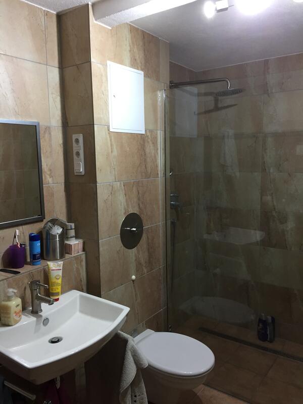 Saniertes Bad mit Waschtisch, Spiegel und Glasabtrennung zur Dusche.