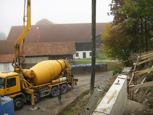 Bau der Gründung: Betonmischer und Pumpe an der Baustelle, Schalung entlang des Hangs.