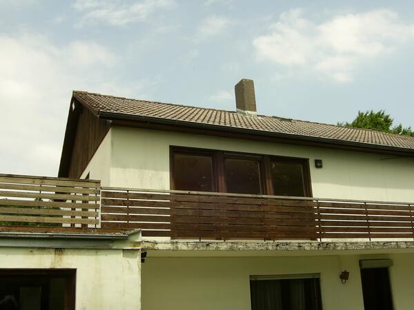 Wohnhaus vor der Sanierung: verwitterter Putz, alte Holzbr&uuml;stung am Balkon, altes Dach.