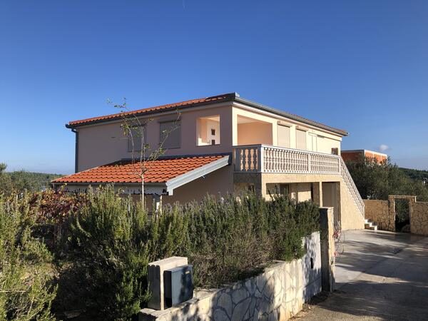 Neubau von außen: zweigeschössiges Haus mit Ziegeldach, Balkon mit Balustrade und mediterraner Bepflanzung.