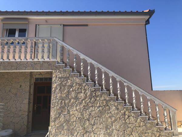 Außentreppe mit Natursteinverkleidung und weißer Balustrade an der Hausfassade.