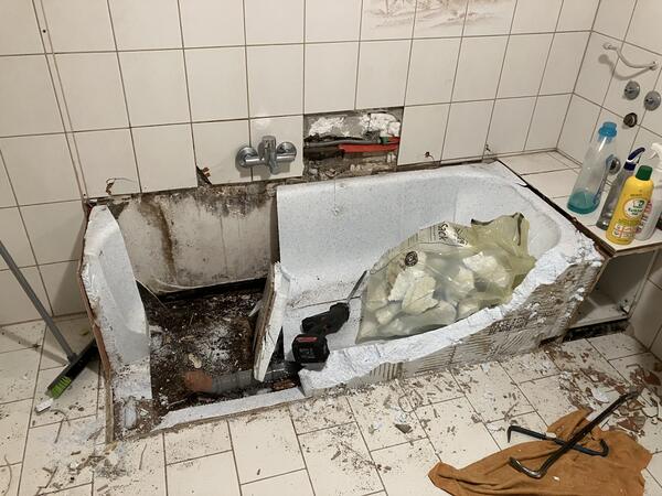 Wasserschaden im Bad: herausgerissene Badewanne, aufgestemmte Wand, Schimmel am Mauerwerk.