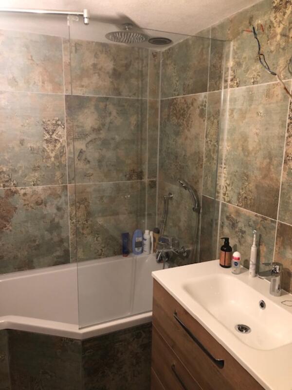 Neue Badewanne mit Holzverkleidung vor der frisch verfliesten Wand.